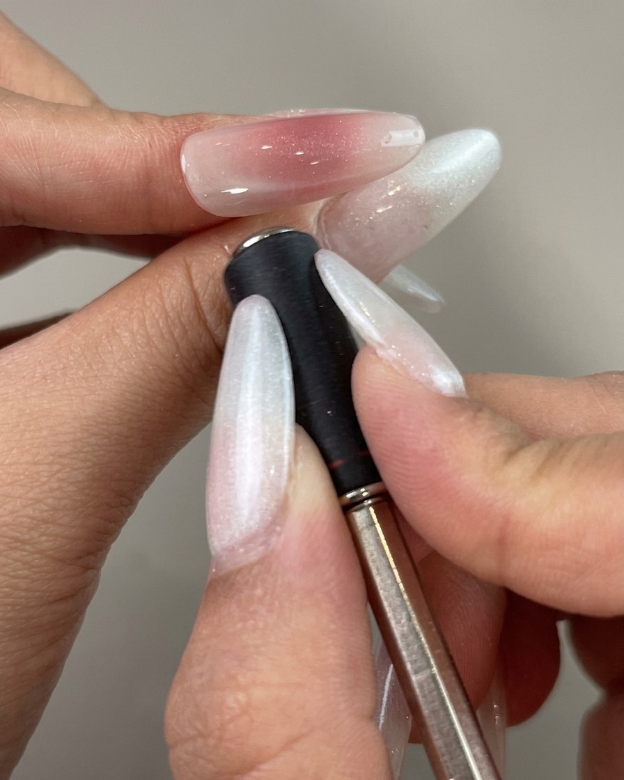 A magnetic wand held close to the side of a painted nail to shape a curved reflection line.