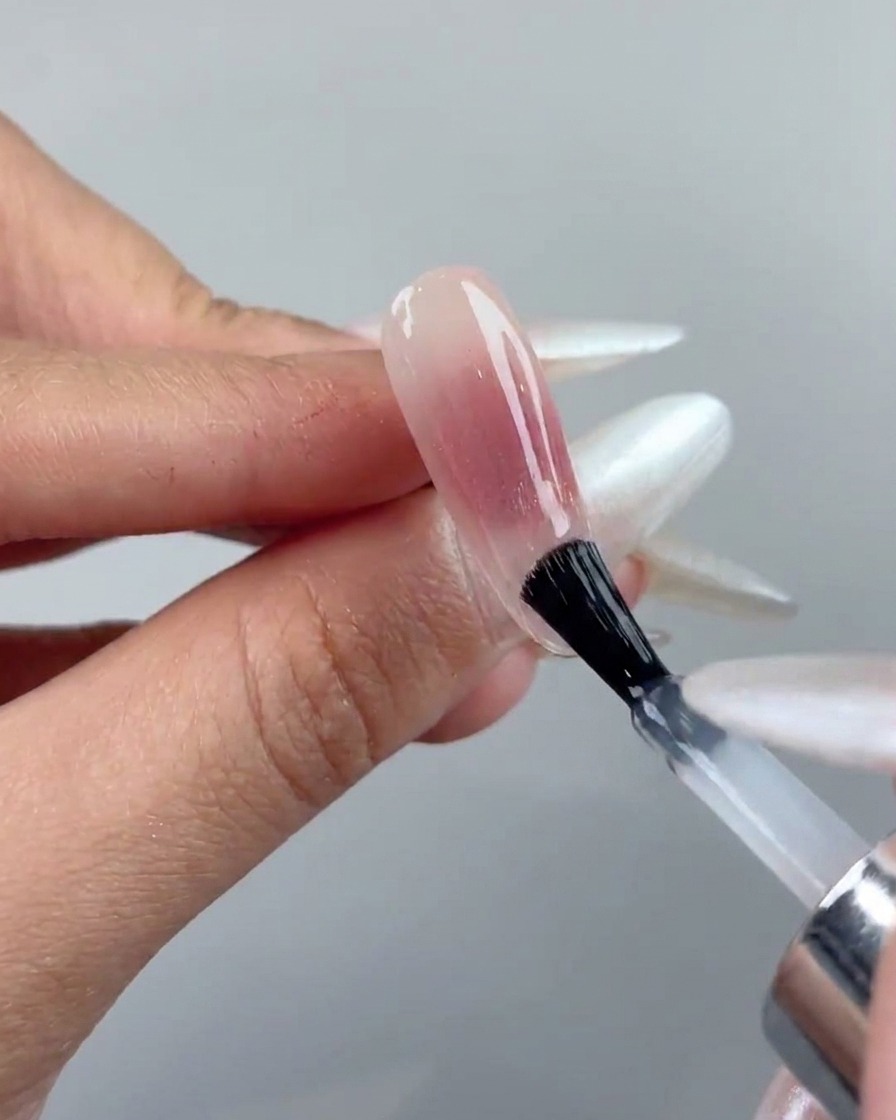 A nail brush applying a clear top coat layer over a cured cat-eye gel nail.
