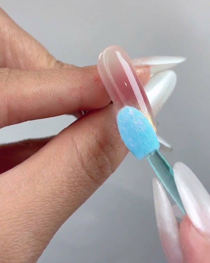 A blue silicone sponge applicator pressing aurora chrome powder onto the tip of a nail.