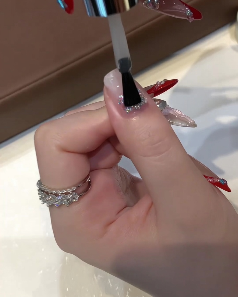A flat gel brush applying a thick layer of clear builder leveling gel over an encapsulated glitter nail.