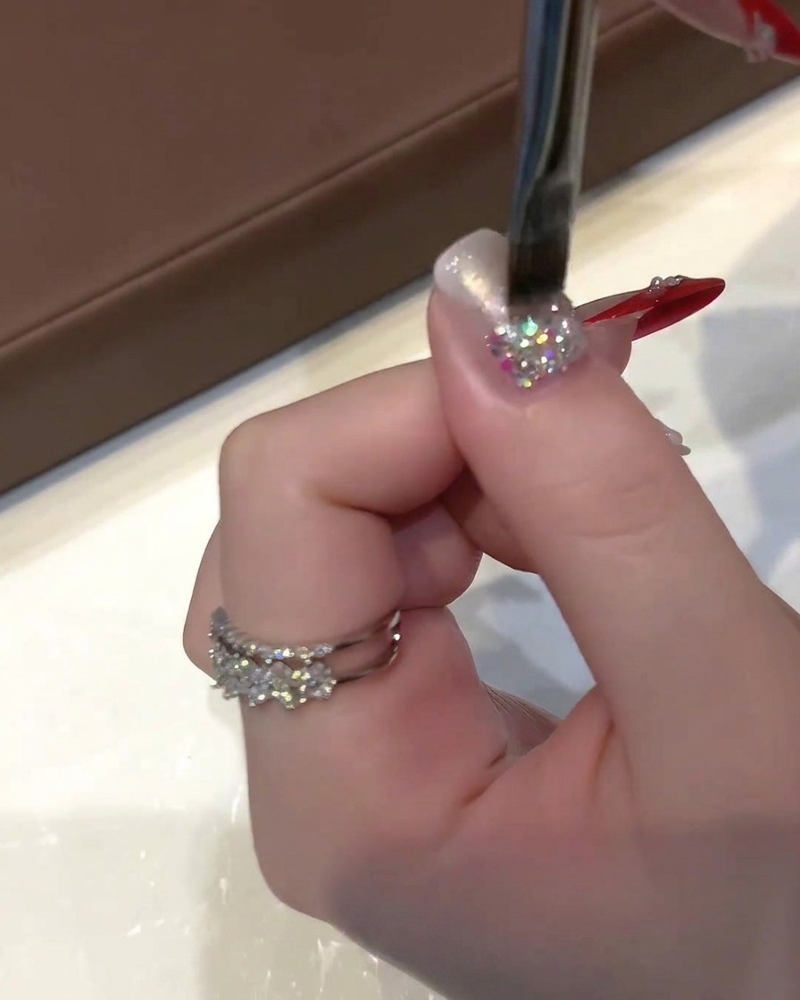 A hand holding a flat gel brush applying sheer cat-eye polish over a glittery nail.