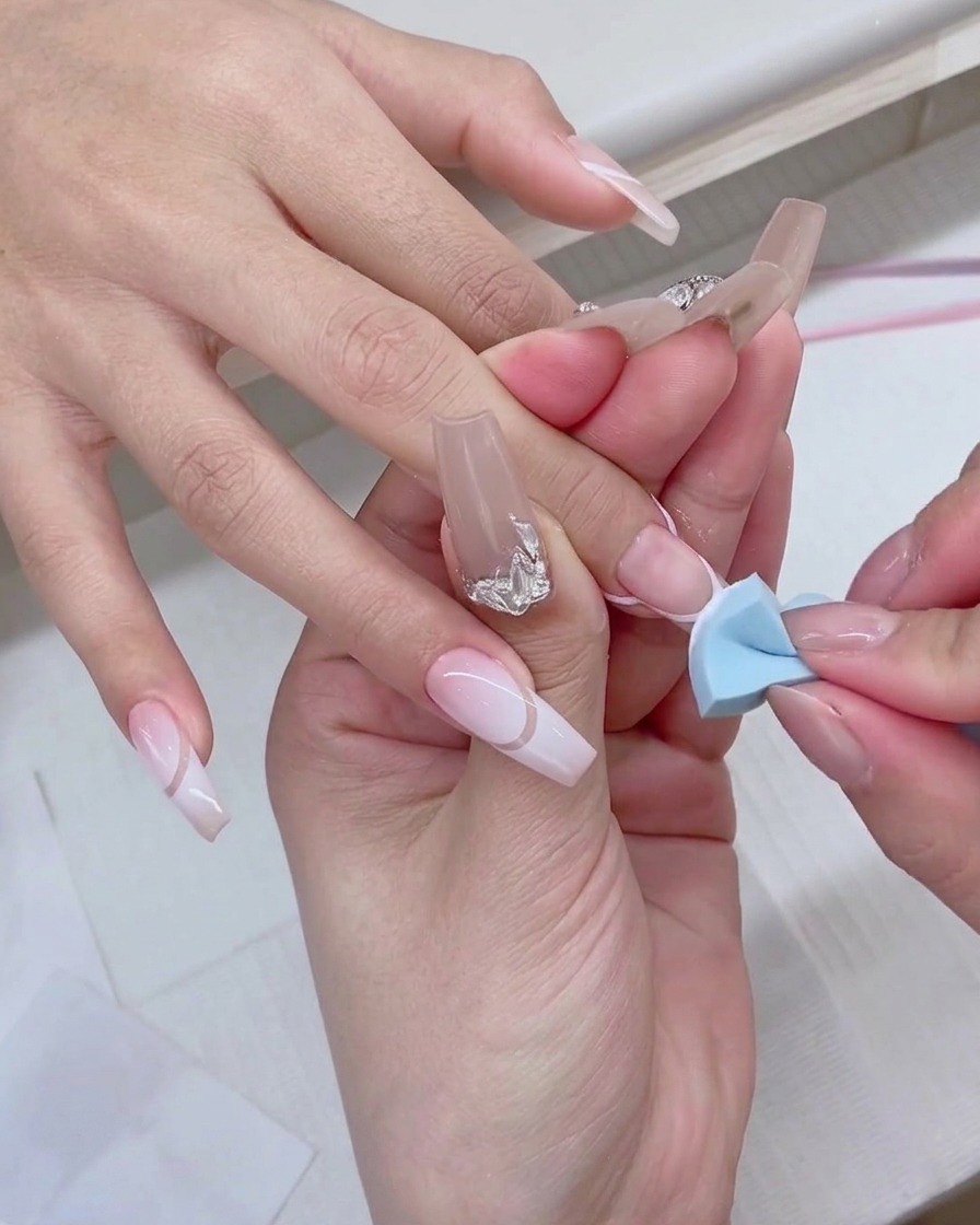 A blue makeup sponge being gently patted onto the tip of a fingernail to create a white gradient effect.