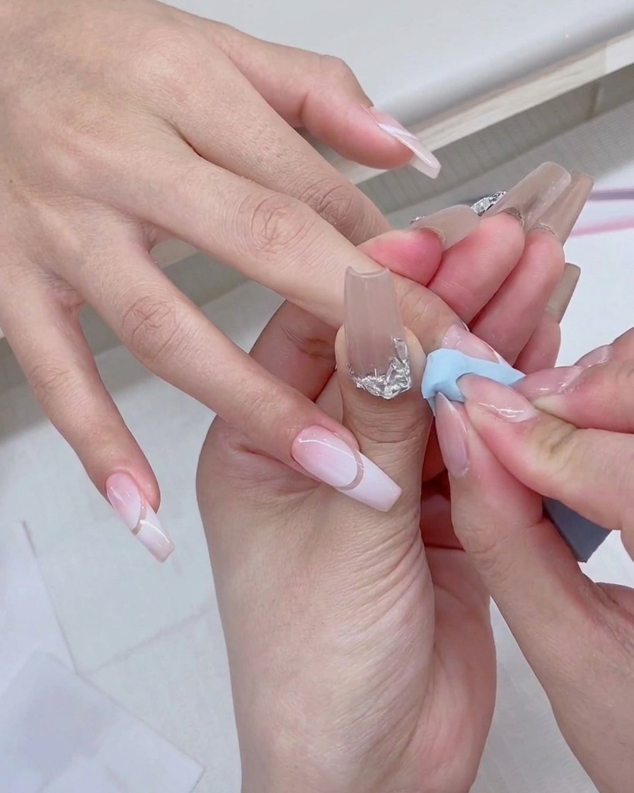 A gel polish brush painting fresh white product directly onto the edge of a blue makeup sponge.