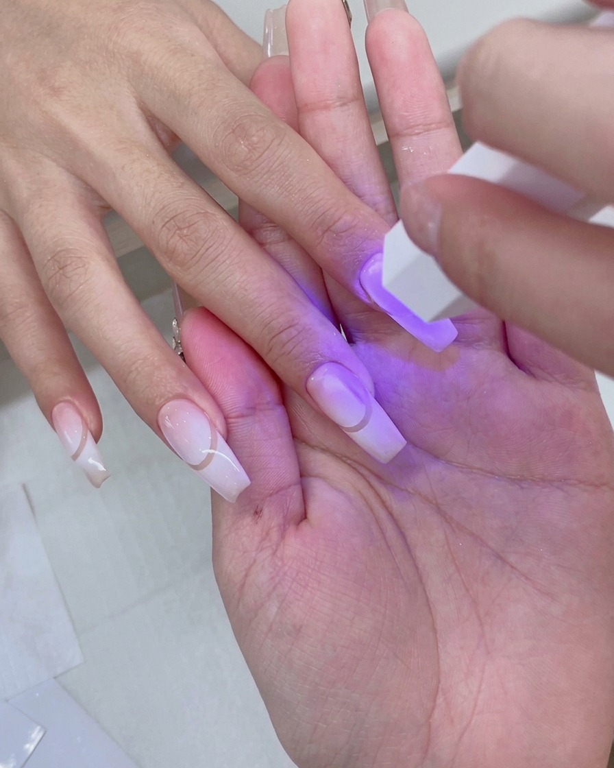 A hand resting inside a pink UV/LED nail lamp with purple light illuminating prepped gradient nails.