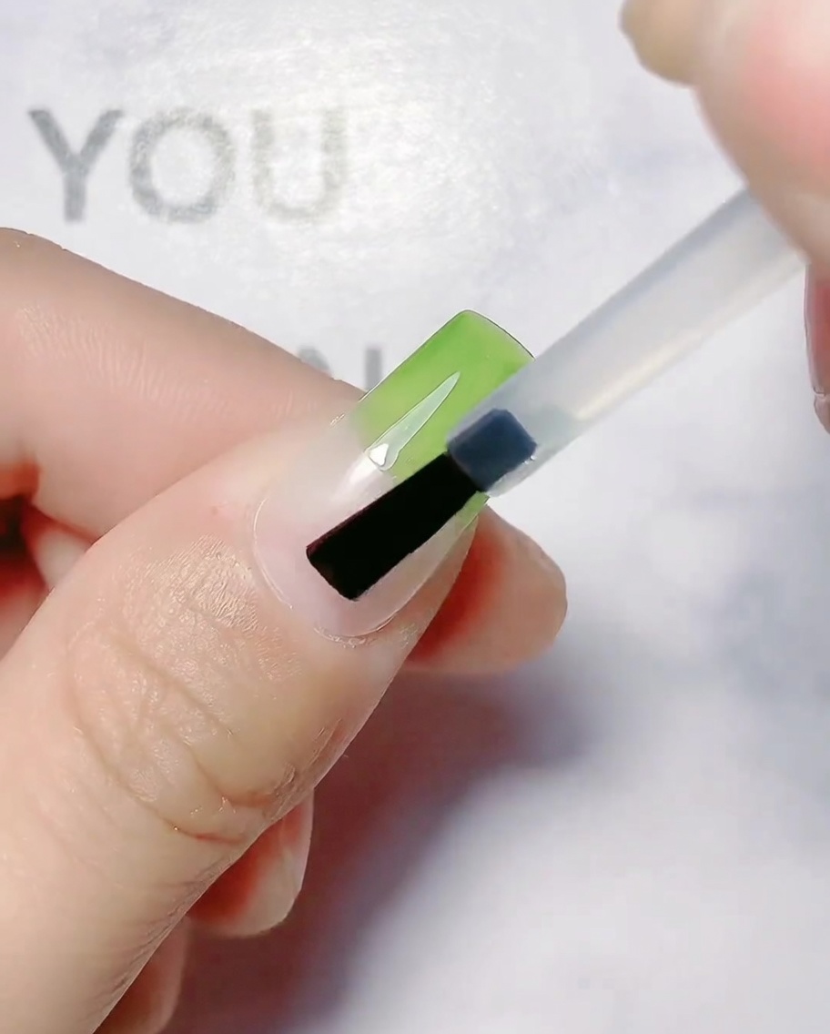 A nail brush applying olive green gel to the upper portion of a natural nail.