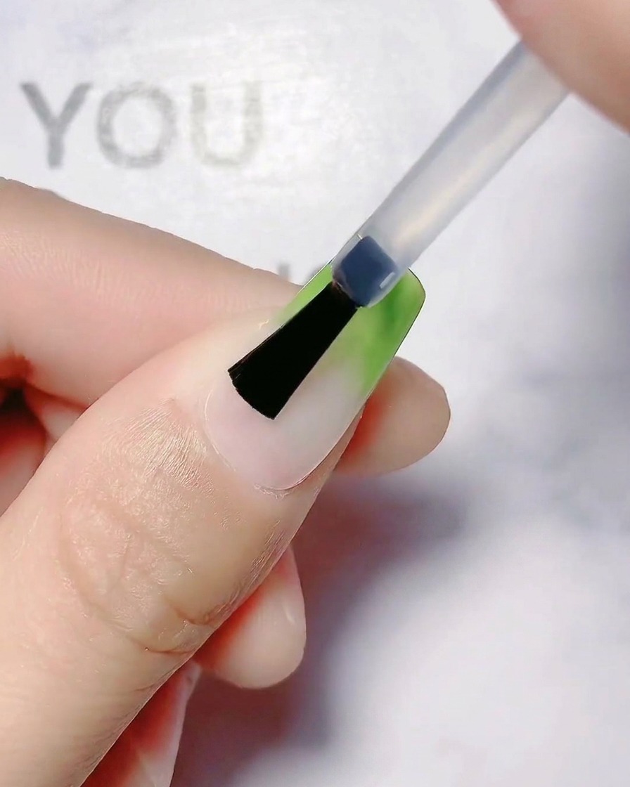 A brush smoothing out the olive green gradient transition on a fingernail.