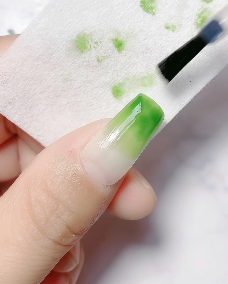 A cleanser pad wiping the sticky inhibition layer off a cured gradient nail.
