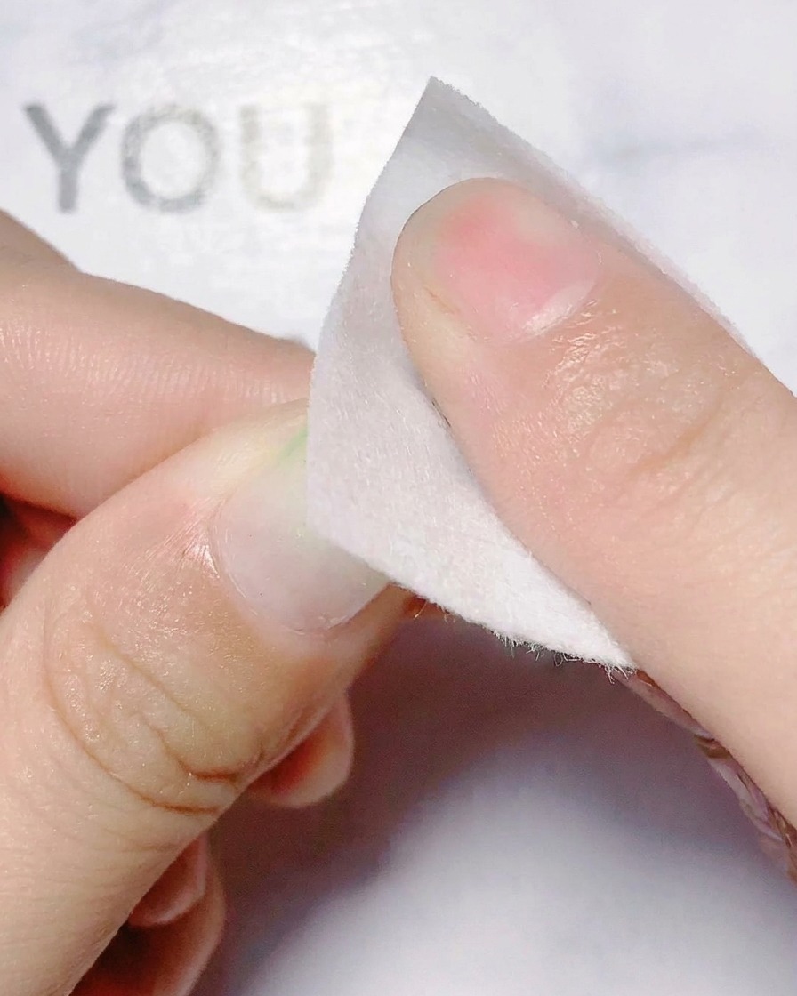 A finger applying a holographic flower cutout sticker onto a fingernail.