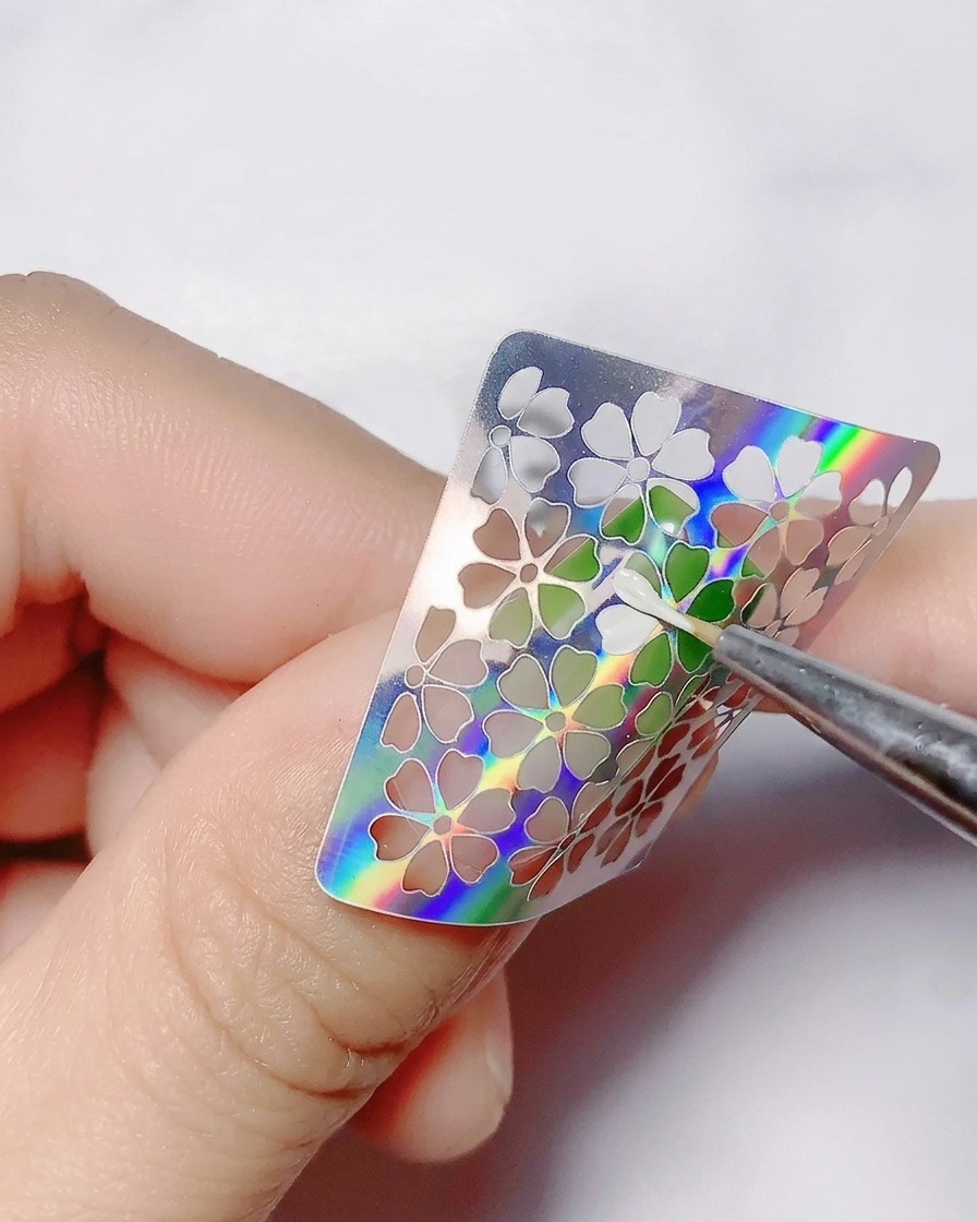 A fine brush applying white color gel inside the hollow flower cutouts of a sticker.