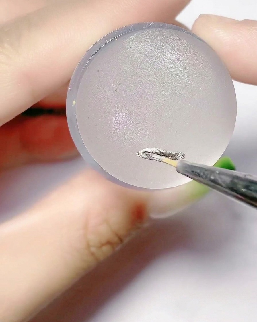 A fine brush applying silver gel onto the flat surface of a silicone stamper pad.