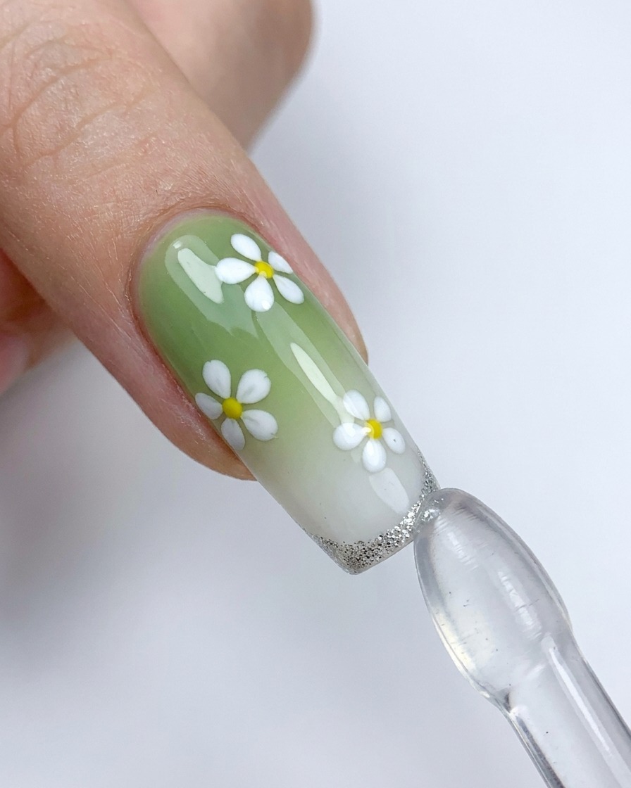 A decorated nail with white flowers being pressed against a silicone stamper to apply a silver French tip.