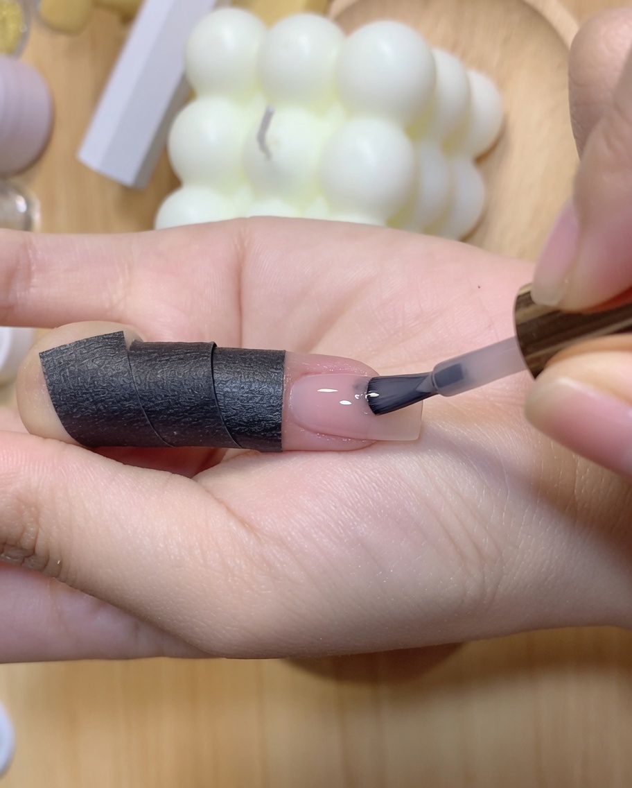 A hand holding a curing lamp over a fingernail receiving its second color coat.