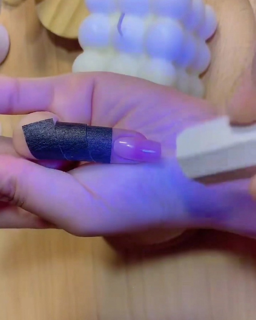 A hand positioned inside a UV/LED nail lamp with blue light illuminating the fingers and cured gradient nail.