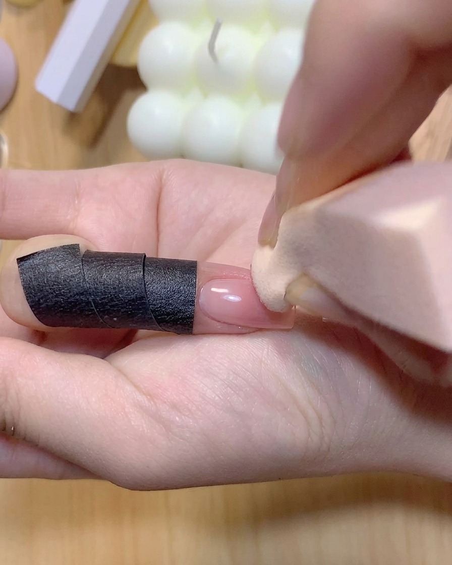 A makeup sponge dabbing pink color onto a manicured fingernail to intensify the ombre gradient.