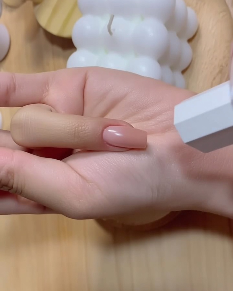 A manicured hand with a deepened pink gradient fingernail positioned near a white UV lamp.