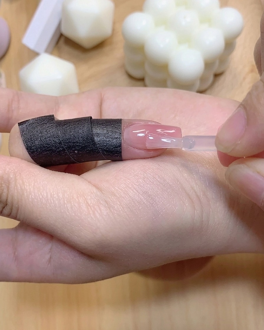 A small brush applying a clear layer of reinforcement gel onto a gradient-colored fingernail.