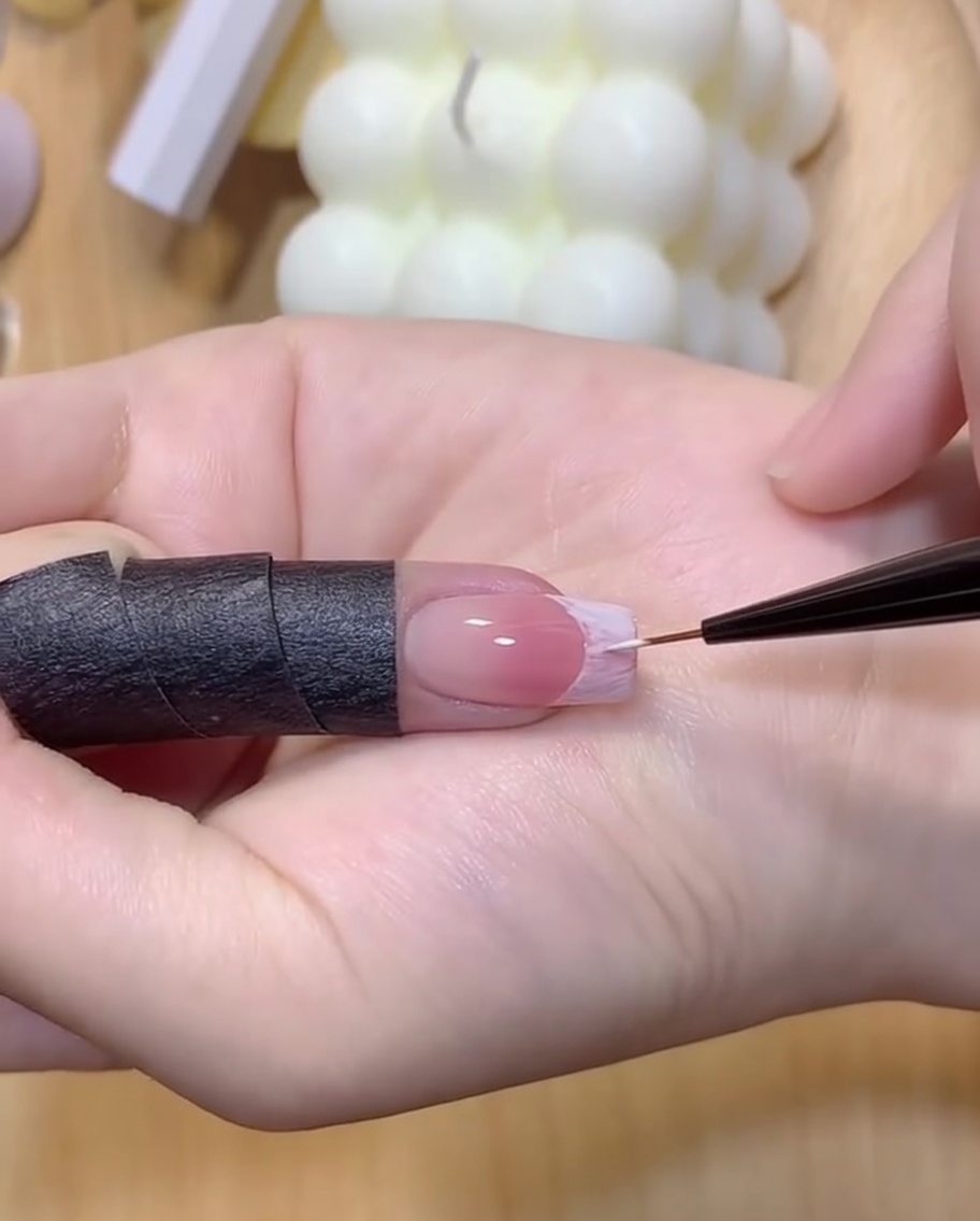 A hand under a UV/LED lamp curing the newly outlined white French nail tip.