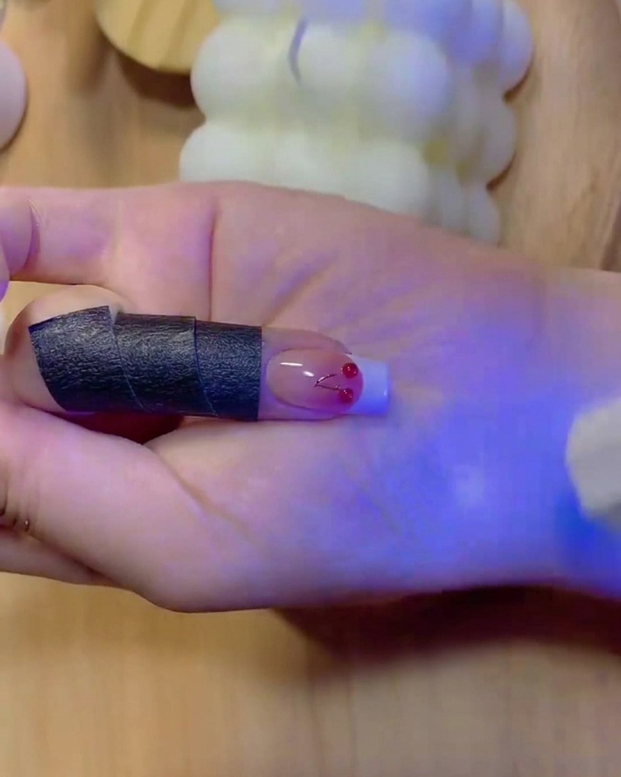 A fine brush filling in the solid white color of a French manicure tip on a gradient nail.