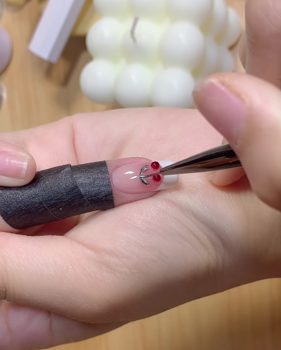 A finger lightly pressing down on two clear gel balls on a nail surface.