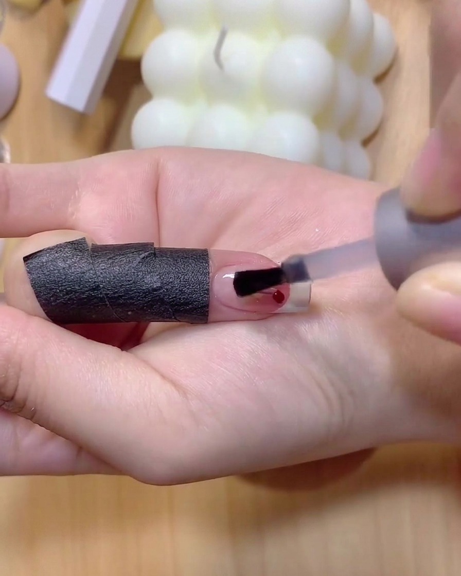 A fine nail brush applying light brown gel polish to draw thin cherry stems on a nail.