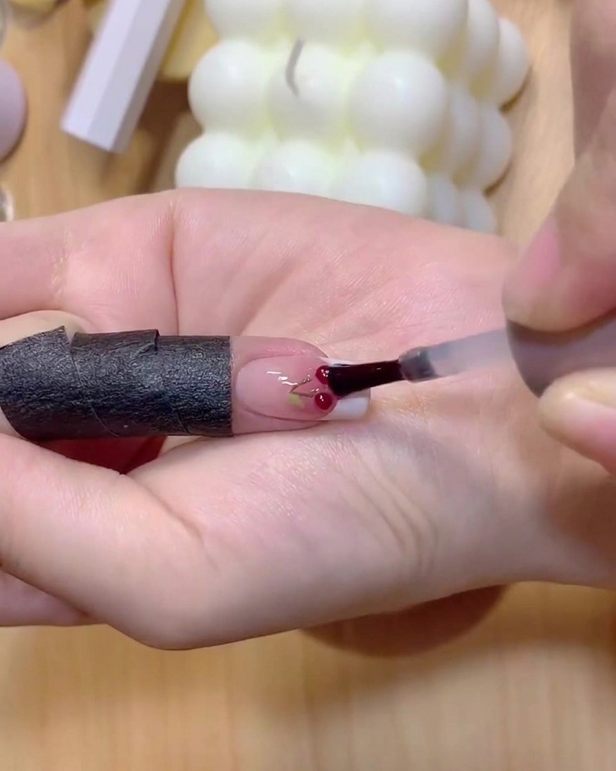 A fingernail with painted cherry stems placed under a curing lamp.