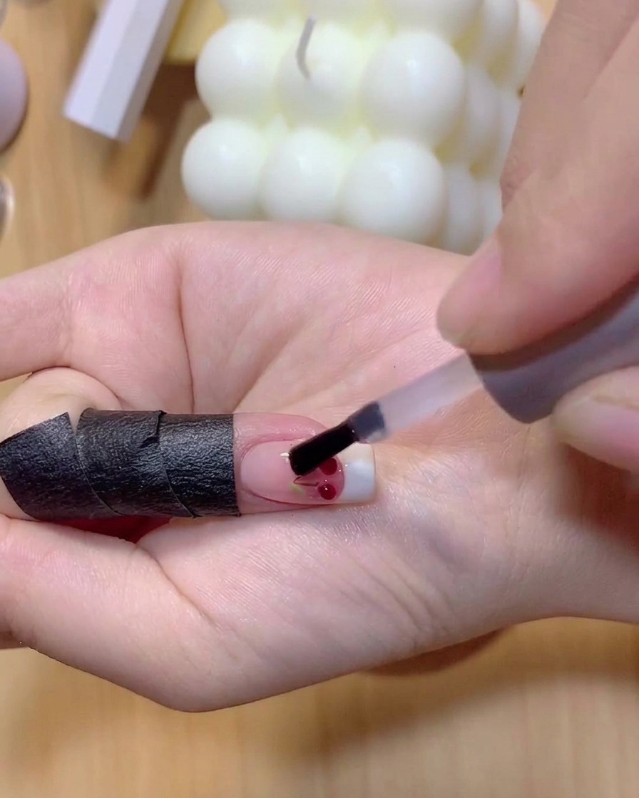 A brush applying translucent red gel polish over the clear 3D cherry balls.