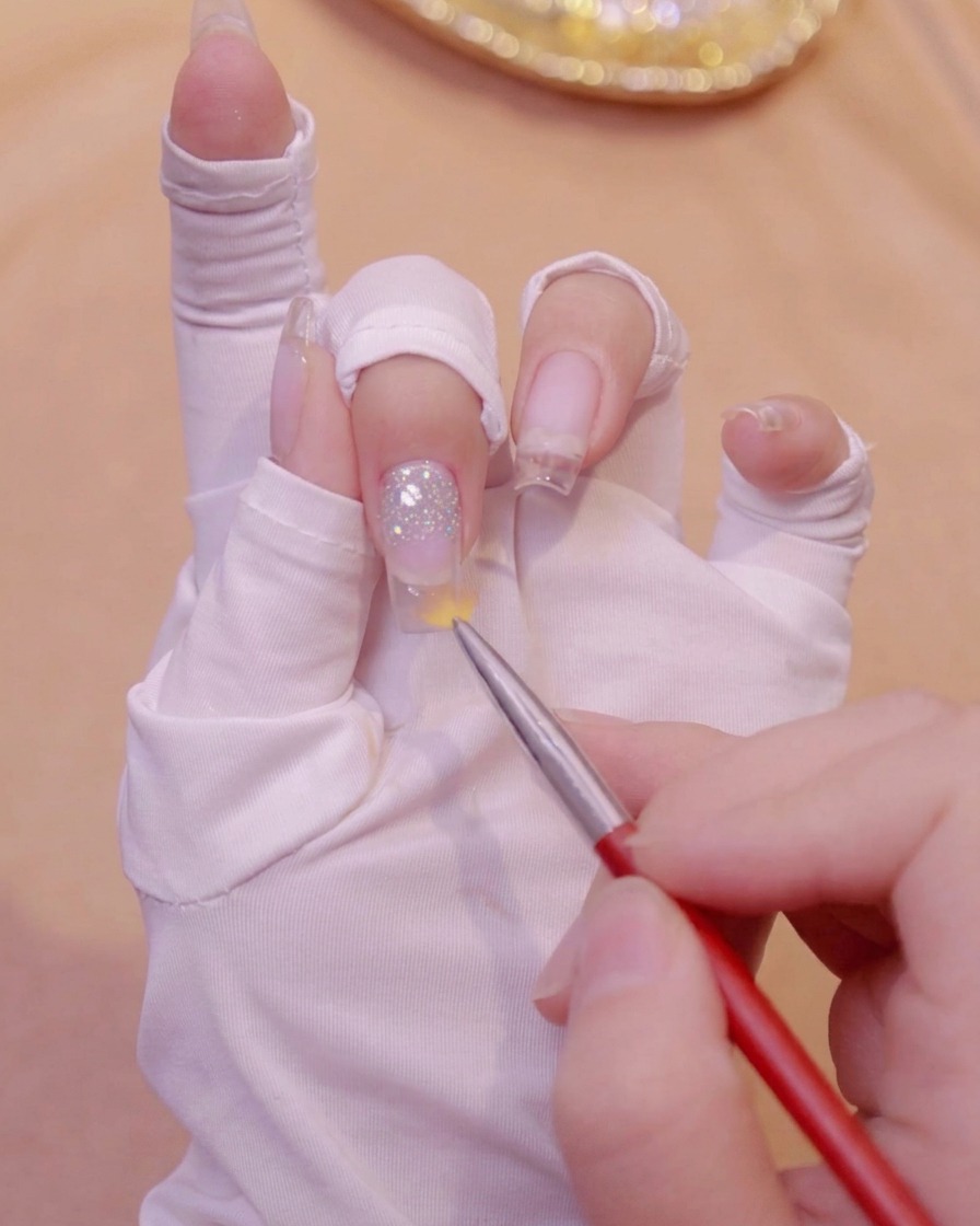 A gradient brush sweeping downward on a clear nail to blend glitter gel.