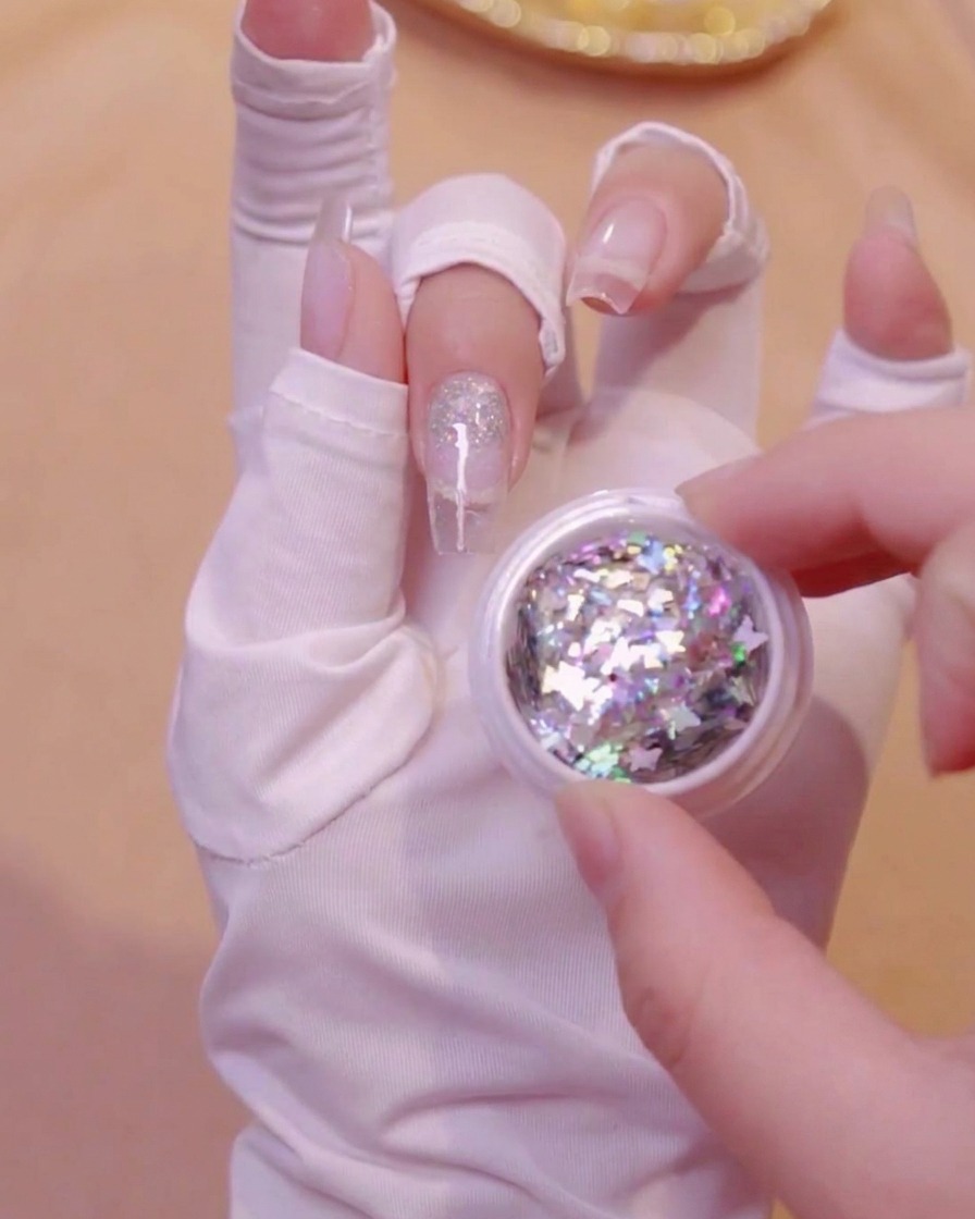 A hand holding an open small jar filled with holographic butterfly glitter sequins.