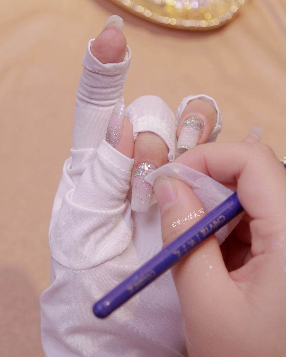 A hand using a wipe to clean around butterfly glitter decorations on a manicured nail.