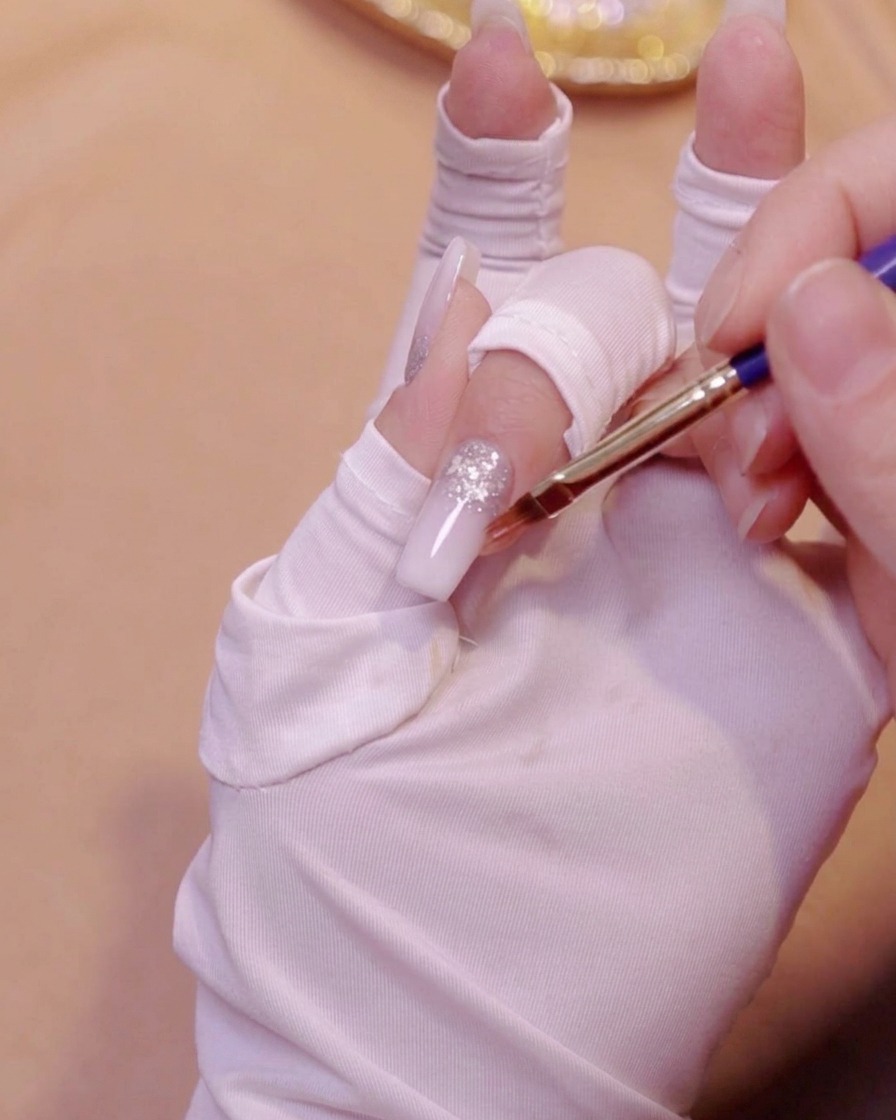 A gradient brush smoothing out the second layer of milky white gel on a nail.