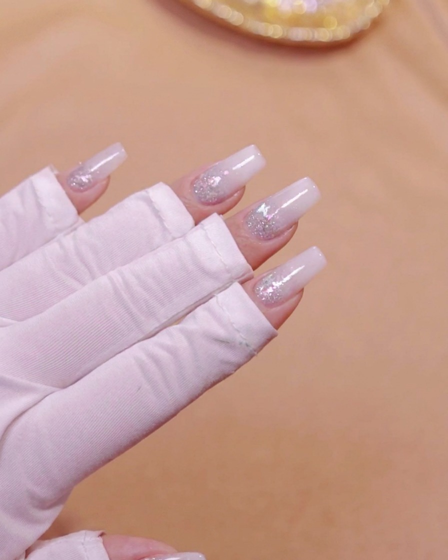 A hand placed inside a UV LED nail lamp curing the milky white gradient layer.