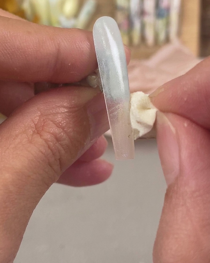 A cosmetic sponge dabbing a secondary color onto the tip of the nail extension to blend the ombre effect.