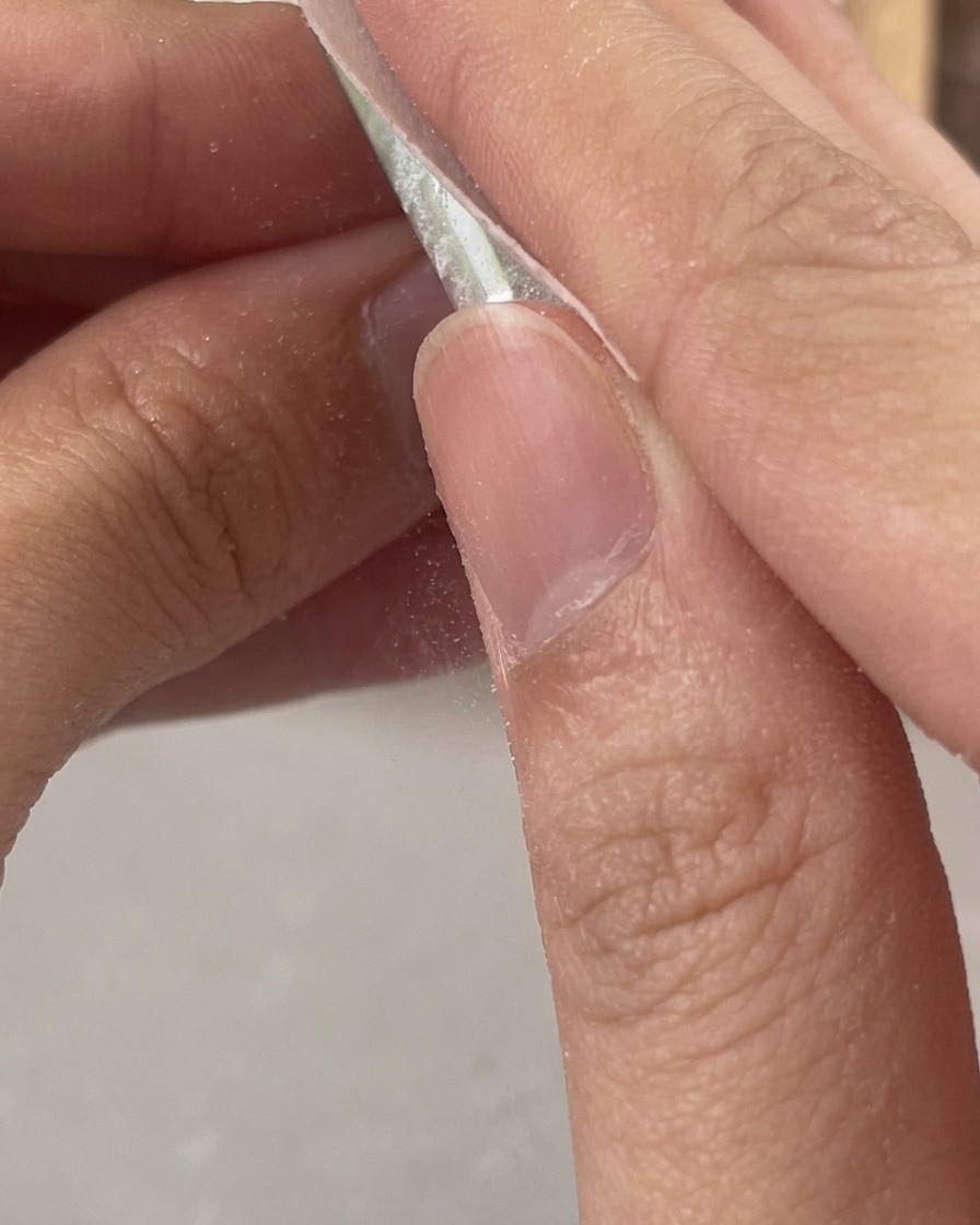 Fingers using a white lint-free wipe to clean the sticky residue off a freshly cured clear gel nail.