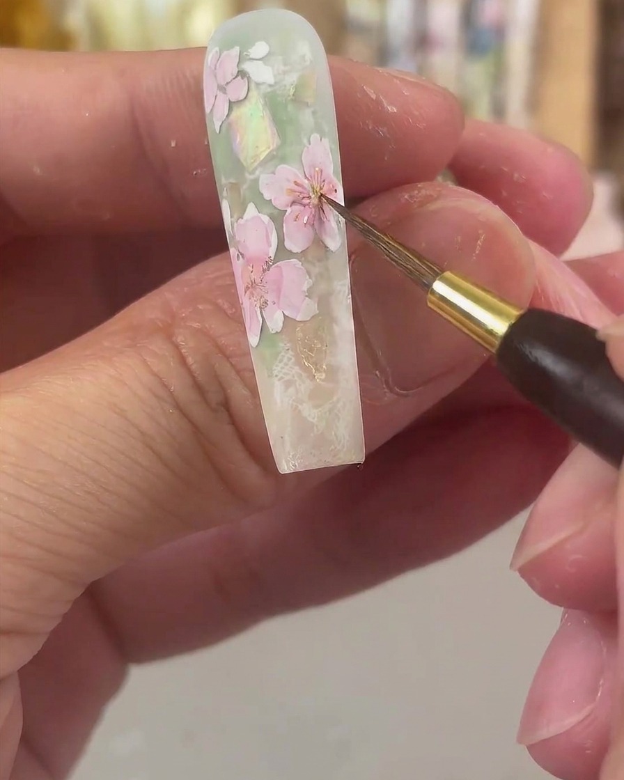 A fine detail brush dabbing bright yellow watercolor into the center of pink-tinted floral petals.