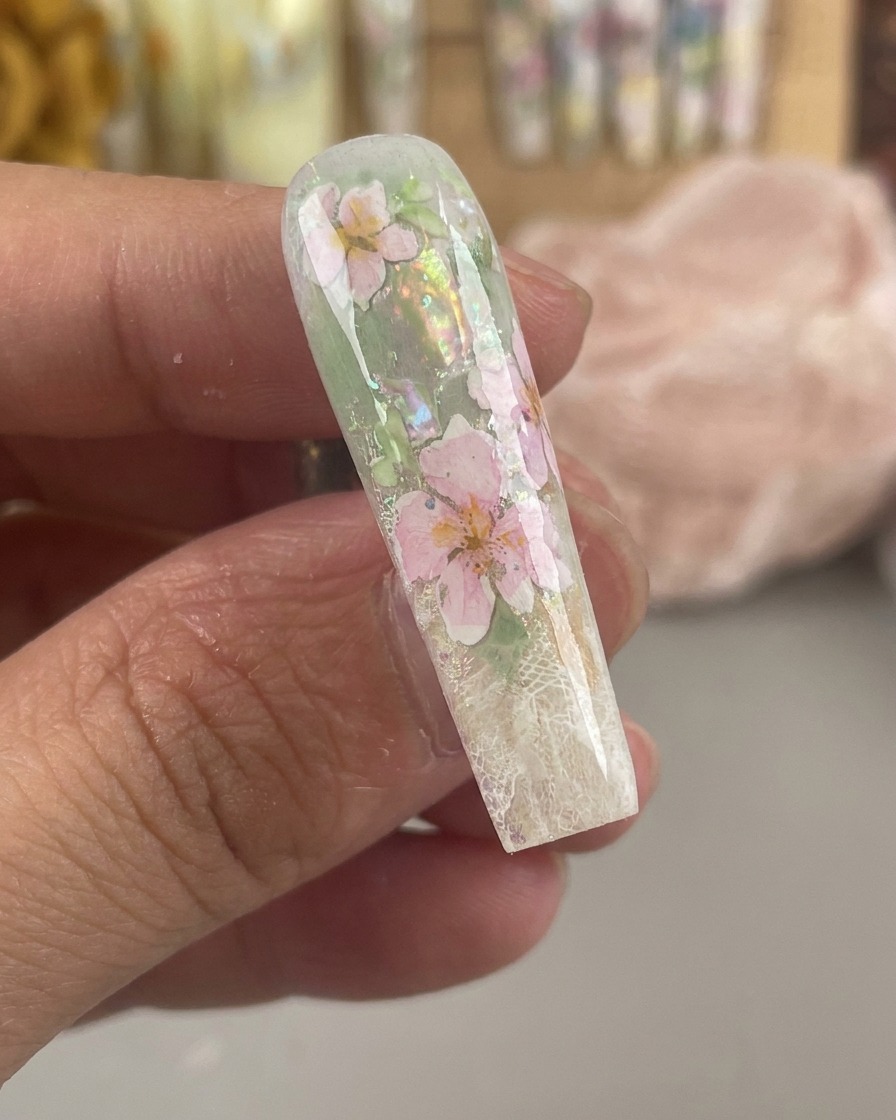 A glossy, encapsulated nail showing sealed pink and yellow watercolor flowers beneath a thick clear gel layer.