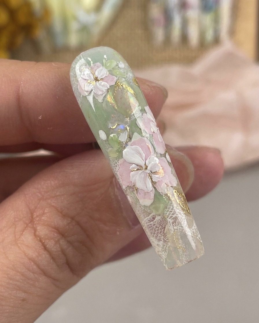 A close-up view of an ultra-fine nail art brush drawing delicate white stamen details and center dots on a floral design.