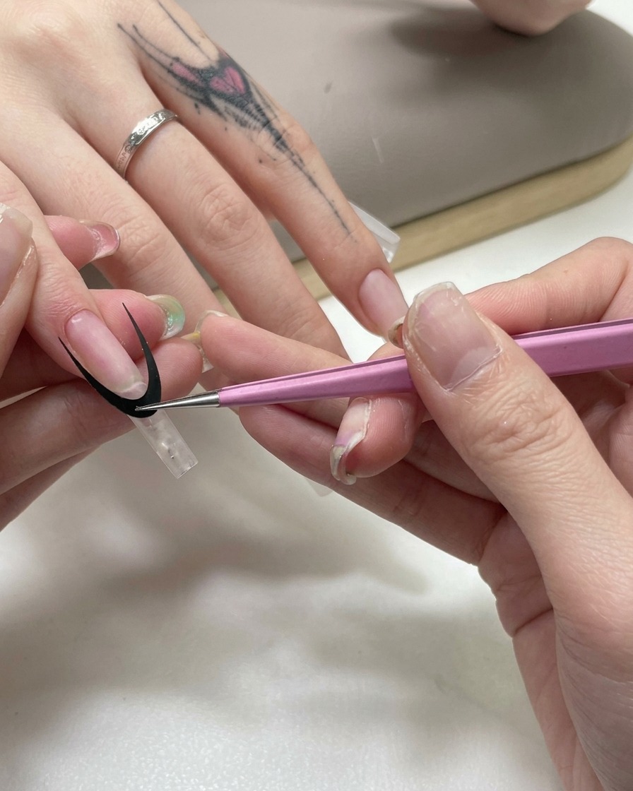 Pink tweezers applying a black curved French tip guide sticker onto a clear nail extension.
