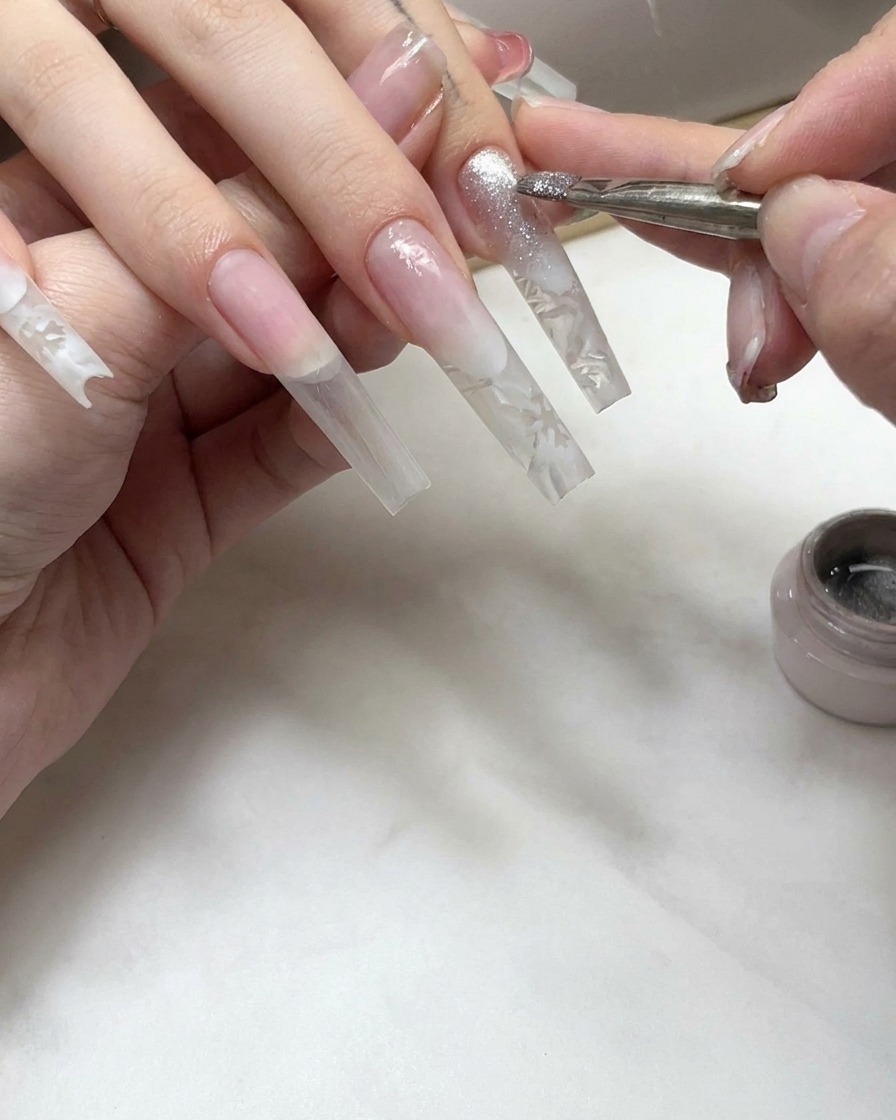 A nail brush applying a shimmering cat-eye gel coat onto the tip section of an extended nail.