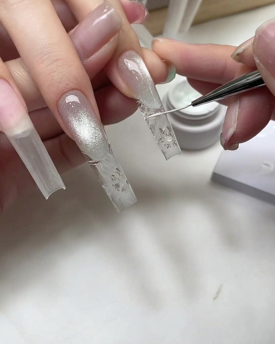 A fine nail art brush drawing white snowflake details onto a clear textured nail extension.
