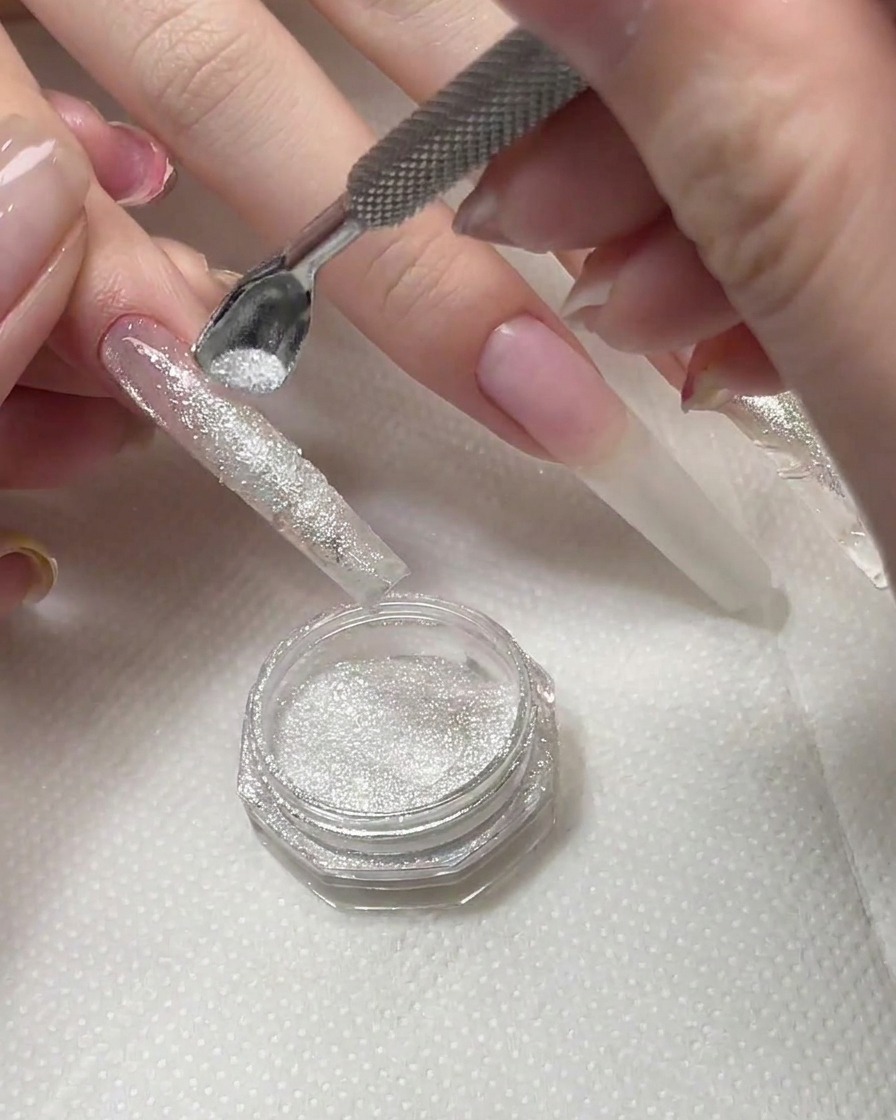A brush sweeping away excess diamond powder from a cured nail surface.