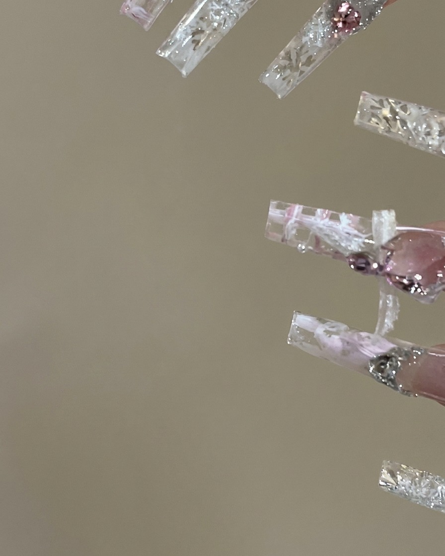 A nail artist applying top coat and carefully brushing colored gel inside the grid sections of a plaid nail design.