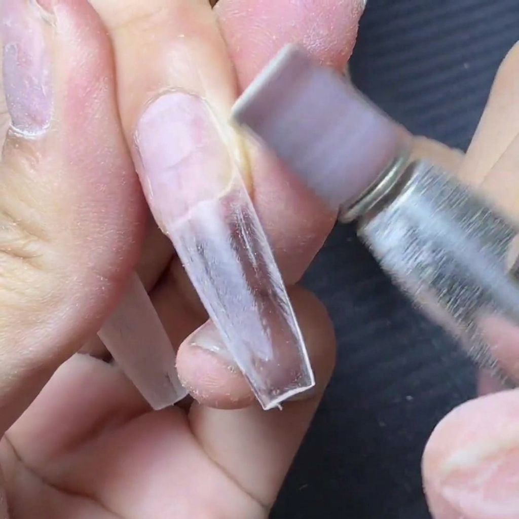 An e-file with a purple sanding band smoothing the connection area of a clear nail extension.