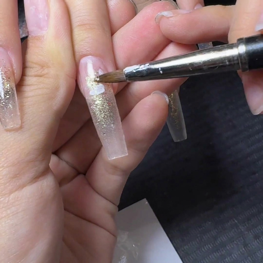 A fine detail brush applying white flower petal designs onto a translucent glitter nail.