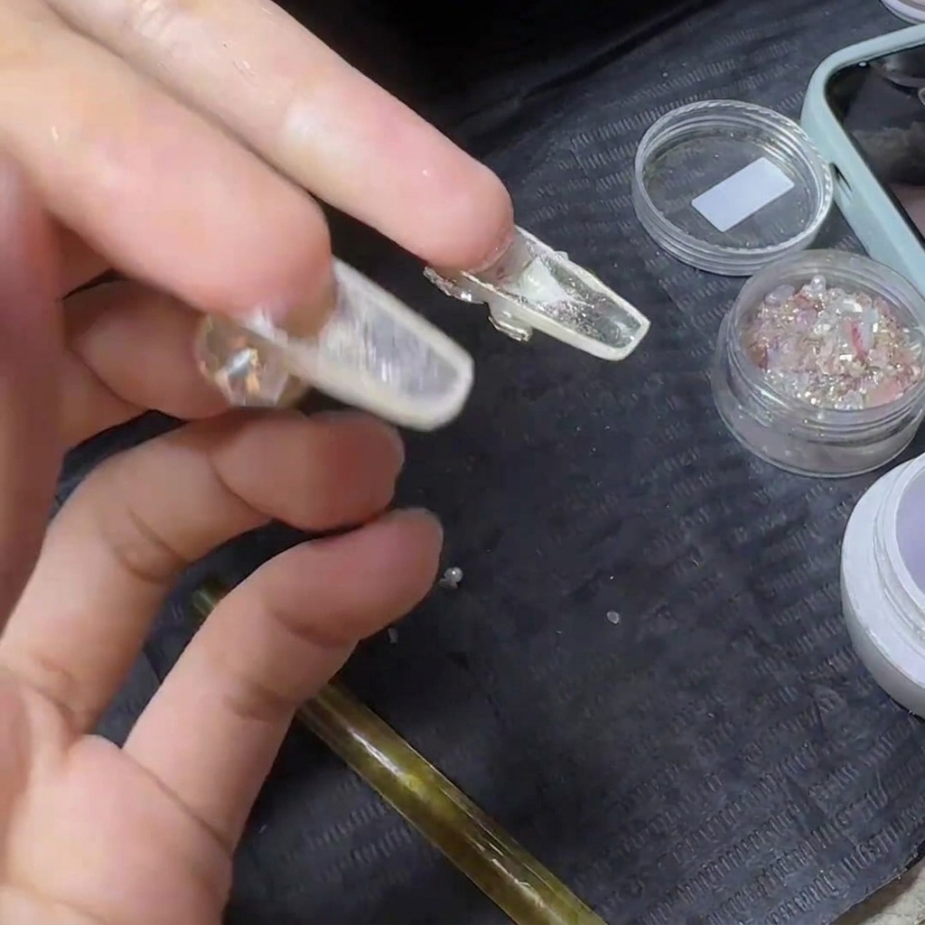 A hand holding a finished clear nail extension turned upside down, exposing the transparent underside for a top coat applicationcite: 1.