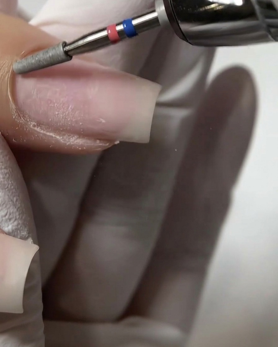 A close-up of a flat cylinder e-file bit gently exfoliating and pushing up the proximal cuticle wall on a natural nail.