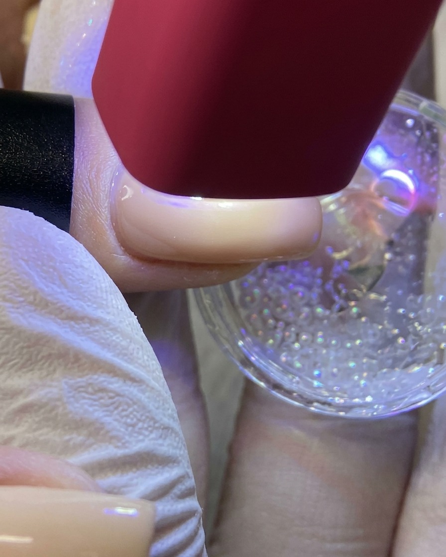 A red handheld UV/LED lamp shining light on a fingernail to cure a white star design coated in glitter.