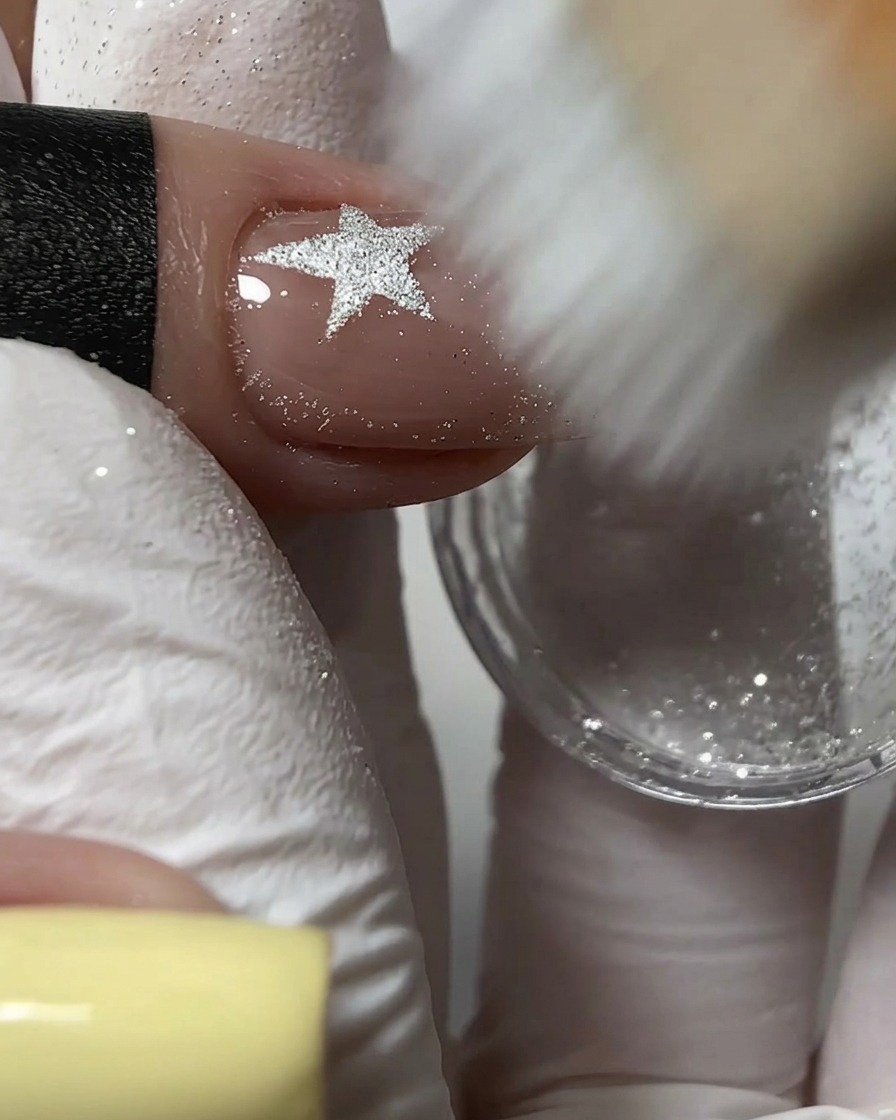 A stiff brush sweeping away excess silver glitter powder from a textured nail design.