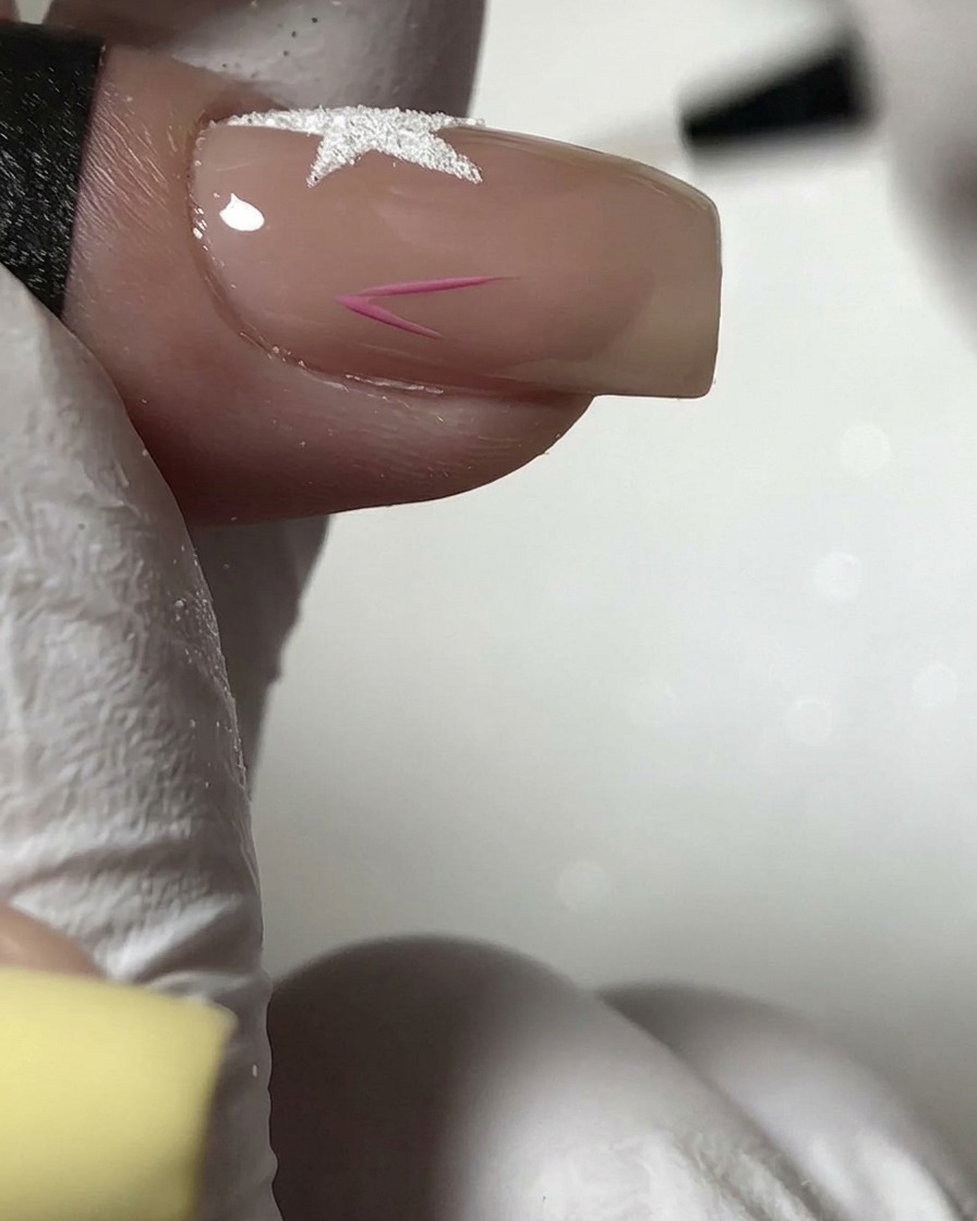 A fine brush painting a small pink star outline on the lower section of a nude nail.