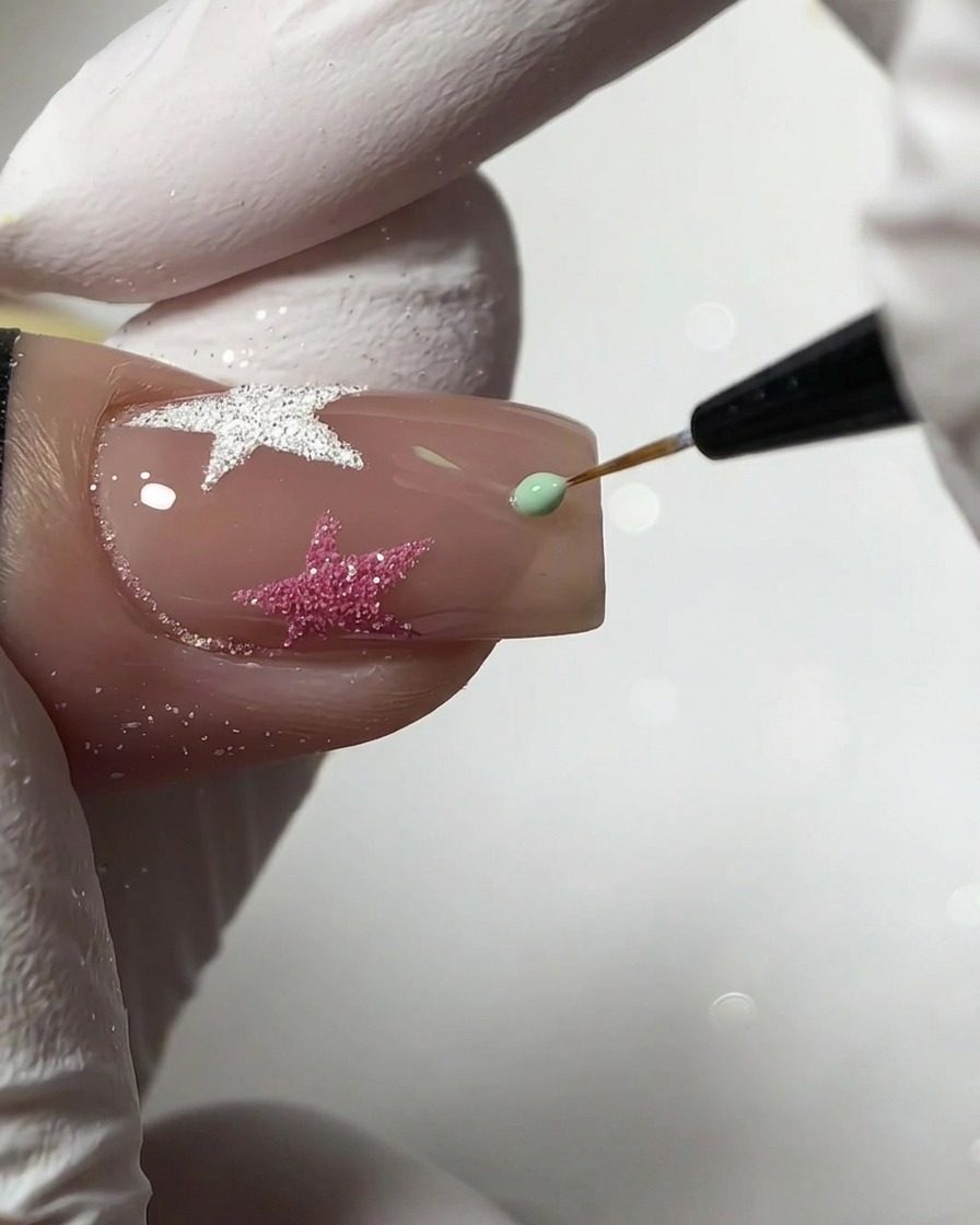 A fine liner brush applying a small drop of mint green gel to create a star shape on a nude nail.