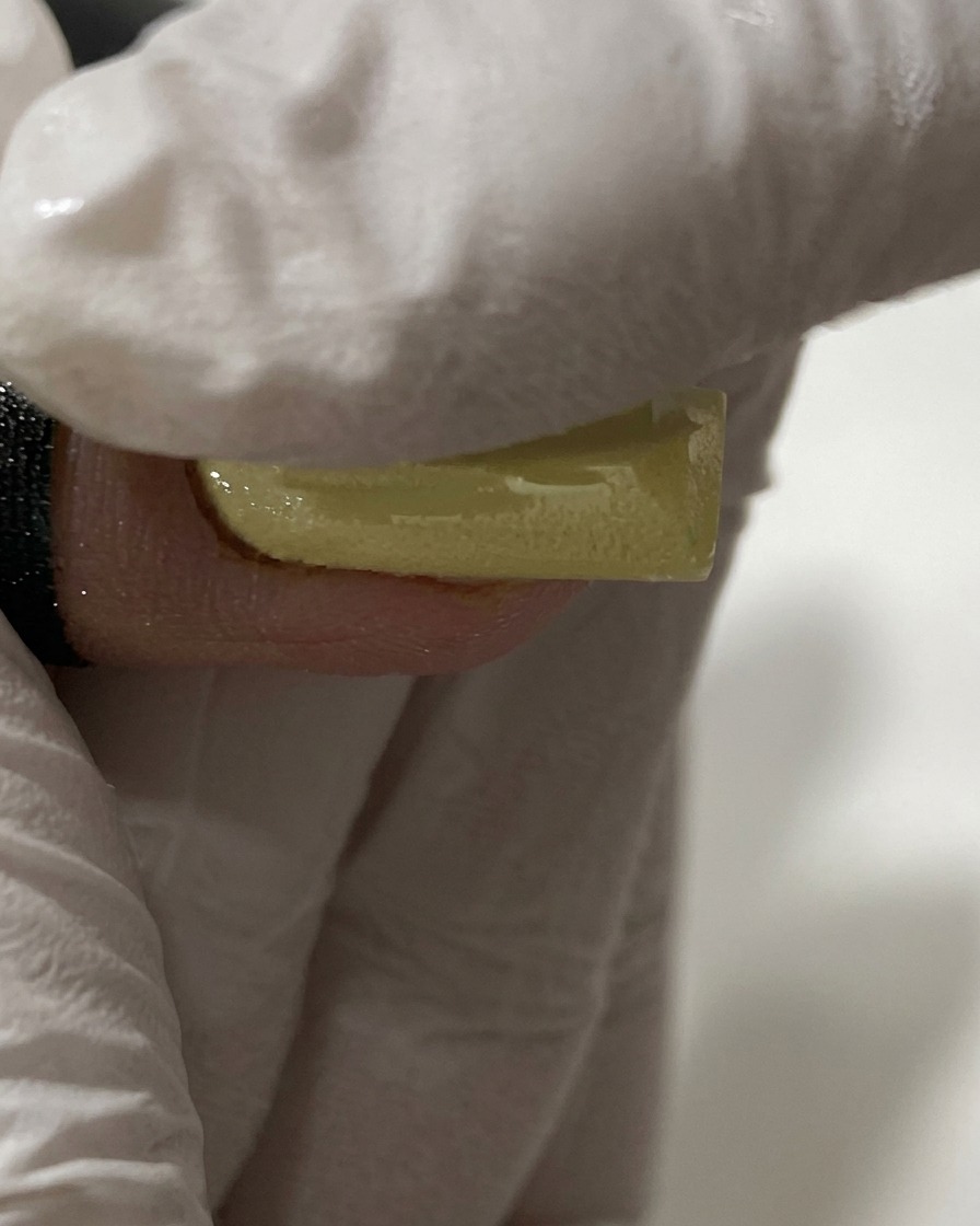 A gloved finger rubbing pearl chrome powder onto a yellow nail.